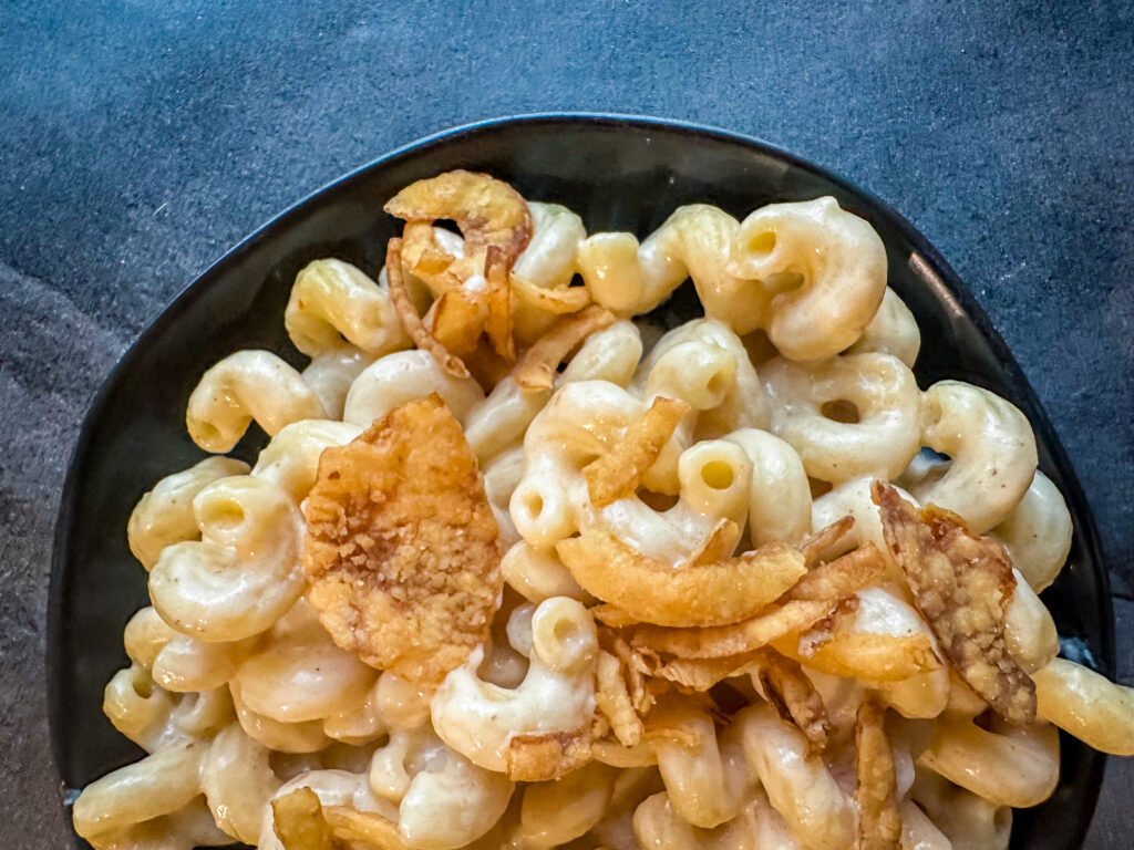 Creamy chipotle mac and cheese in a black bowl topped with crispy onions on a dark stone background.