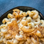 Creamy chipotle mac and cheese in a black bowl topped with crispy onions on a dark stone background.