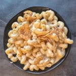 Creamy macaroni and cheese with crispy fried onions in a black bowl, showcasing classic comfort food from the Mac and Cheese Club.