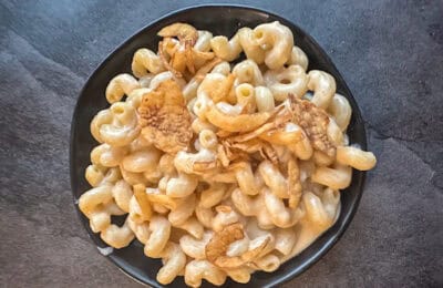 Creamy macaroni and cheese with crispy fried onions in a black bowl, showcasing classic comfort food from the Mac and Cheese Club.
